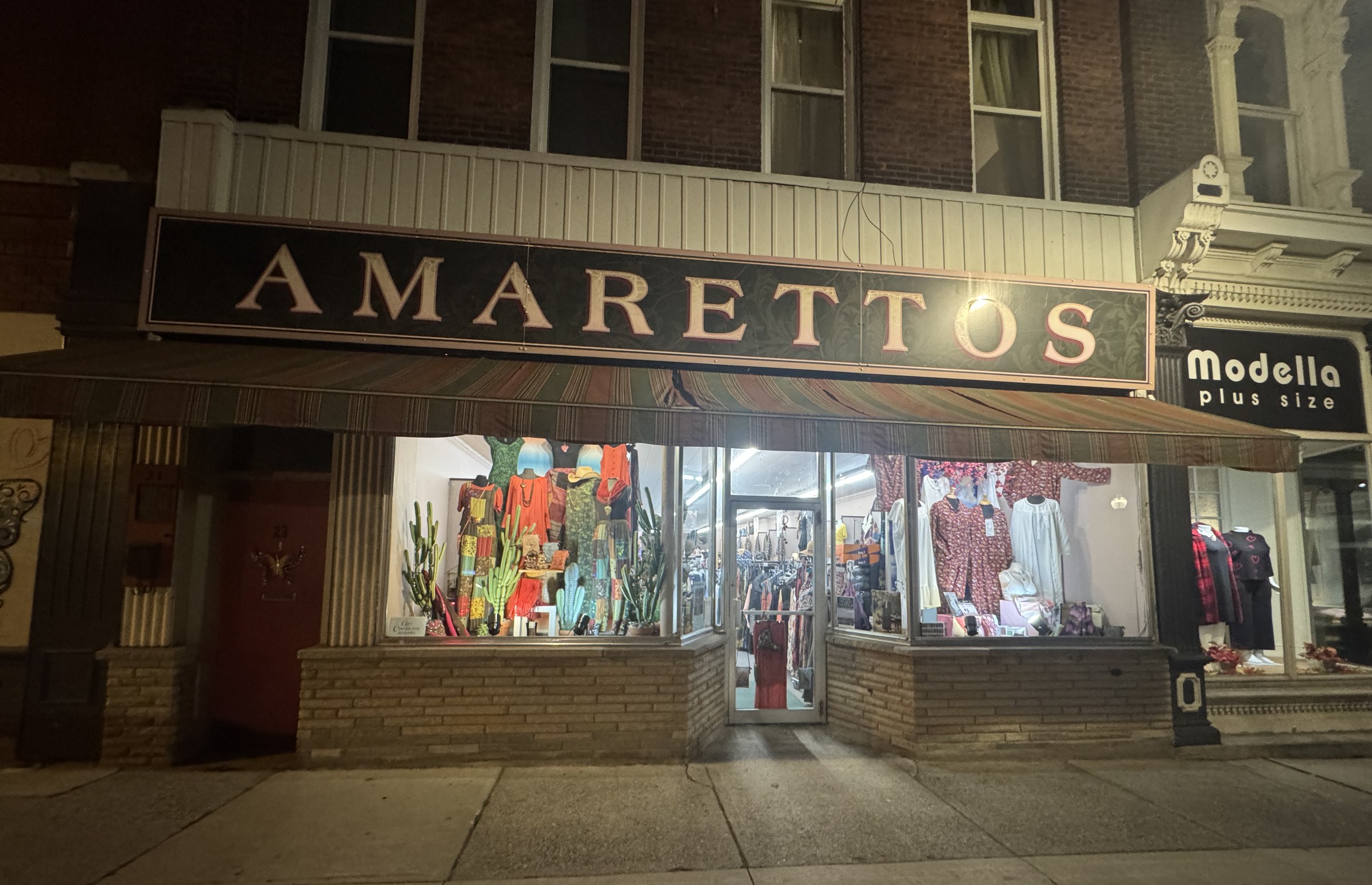 The Amarettos storefront at 21 King St W in Dundas at night, gold lettering on a black sign above a striped awning and two lit display windows